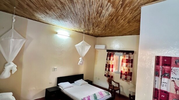 A bedroom with a bed, bedside tables, a chair, a mosquito net, and a curtain with a zebra pattern.