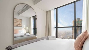 Habitación de hotel con una cama grande, vistas a la ciudad, un espejo y una obra de arte enmarcada en la pared.