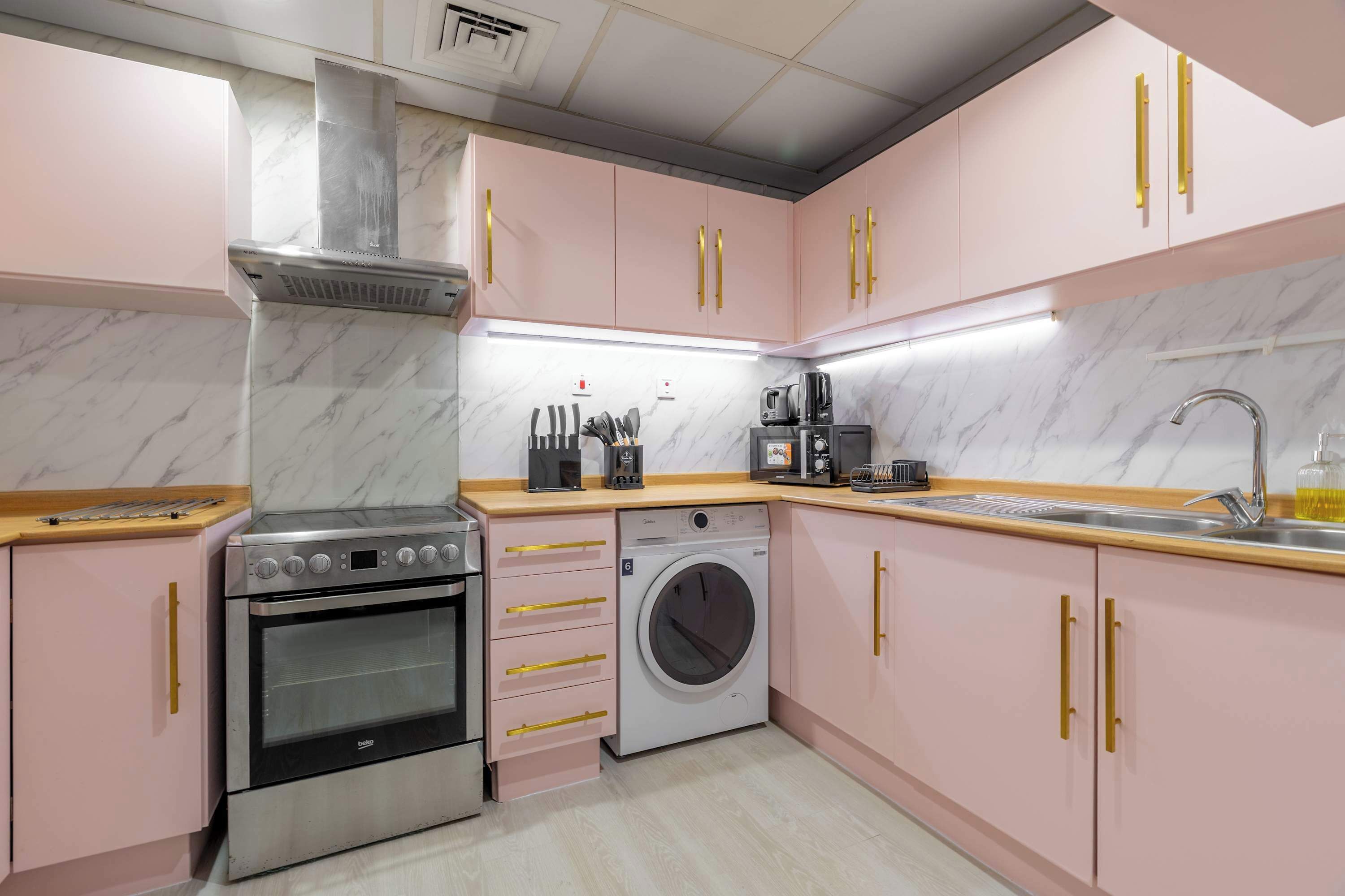 Una cucina con mobili rosa, un forno in acciaio inossidabile, una lavatrice e una macchina da caffè.