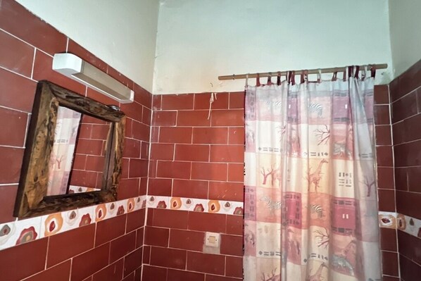 A bathroom with red tiled walls, a wooden-framed mirror, and a zebra-patterned shower curtain.