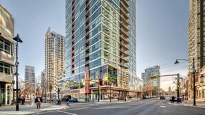 A high-rise building with multiple floors, large windows, and a pedestrian walkway on the ground level. - DT Views | UG Park | Walk to Saddledome (Calgary)