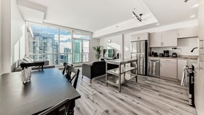 A modern apartment with a dining area, kitchen, and large windows offering city views. - DT Views | UG Park | Walk to Saddledome (Calgary)
