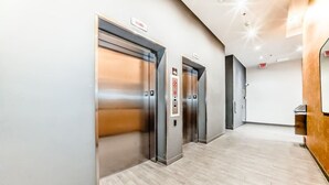 A modern elevator area with three elevators, a wooden reception desk, and a light-colored floor. - DT Views | UG Park | Walk to Saddledome (Calgary)