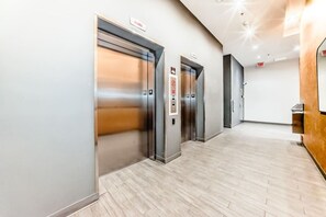 Ein moderner Aufzugsbereich mit drei Aufzügen, einem Holzbüro und einem hellen Boden.