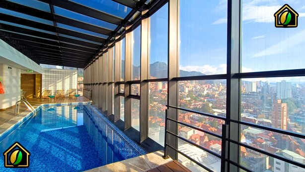 A modern indoor swimming pool with large windows offering a city view. - Penthouse in Zona T with Rooftop Pool, Sauna & Gym (Bogotá)