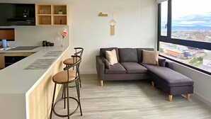 A modern living space with a kitchen area, a gray sectional sofa, and a bar stool seating arrangement. - Penthouse in Zona T with Rooftop Pool, Sauna & Gym (Bogotá)