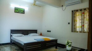 Ein Schlafzimmer mit einem Bett, einem kleinen Tisch, einer Blumenvase, einem Deckenventilator und einer Klimaanlage.