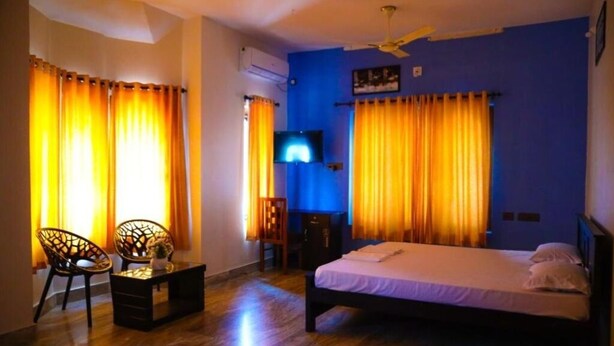 A bedroom with a bed, two chairs, a small table, a TV, and curtains.