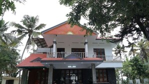 A two-story building with a balcony, a fountain in front, and palm trees around. - Ocean Queen Palace Poovar – Double Room with Refreshing Pool Views (Poovar)