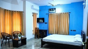 A bedroom with a bed, a desk, two chairs, a TV, and curtains. - Ocean Queen Palace Poovar – Double Room with Refreshing Pool Views (Poovar)
