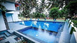 A swimming pool with a tiled deck, surrounded by palm trees and greenery.