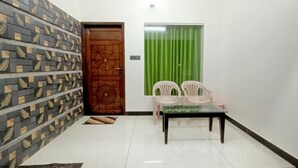 A room with a patterned wall, a wooden door, a green curtain, a table with chairs, and a ceiling fan.