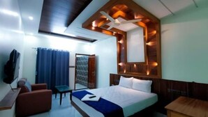A modern hotel room with a large bed, a desk, a chair, and a TV.