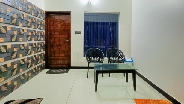 A small dining area with a glass table and two chairs, a patterned wall, a wooden door, and a blue curtain.
