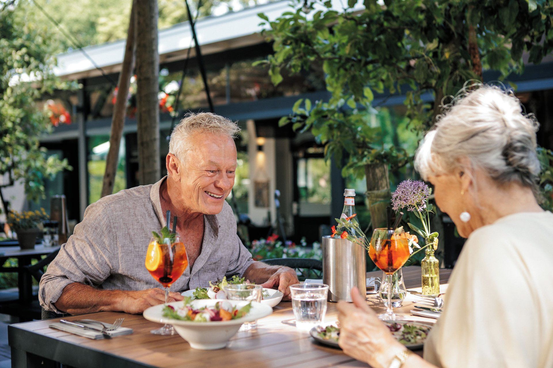 An outdoor dining area with tables, chairs, and a variety of table settings including plates, glasses, and a bottle.