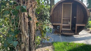 Una struttura a forma di botte in legno con una porta, circondata da alberi e erba.