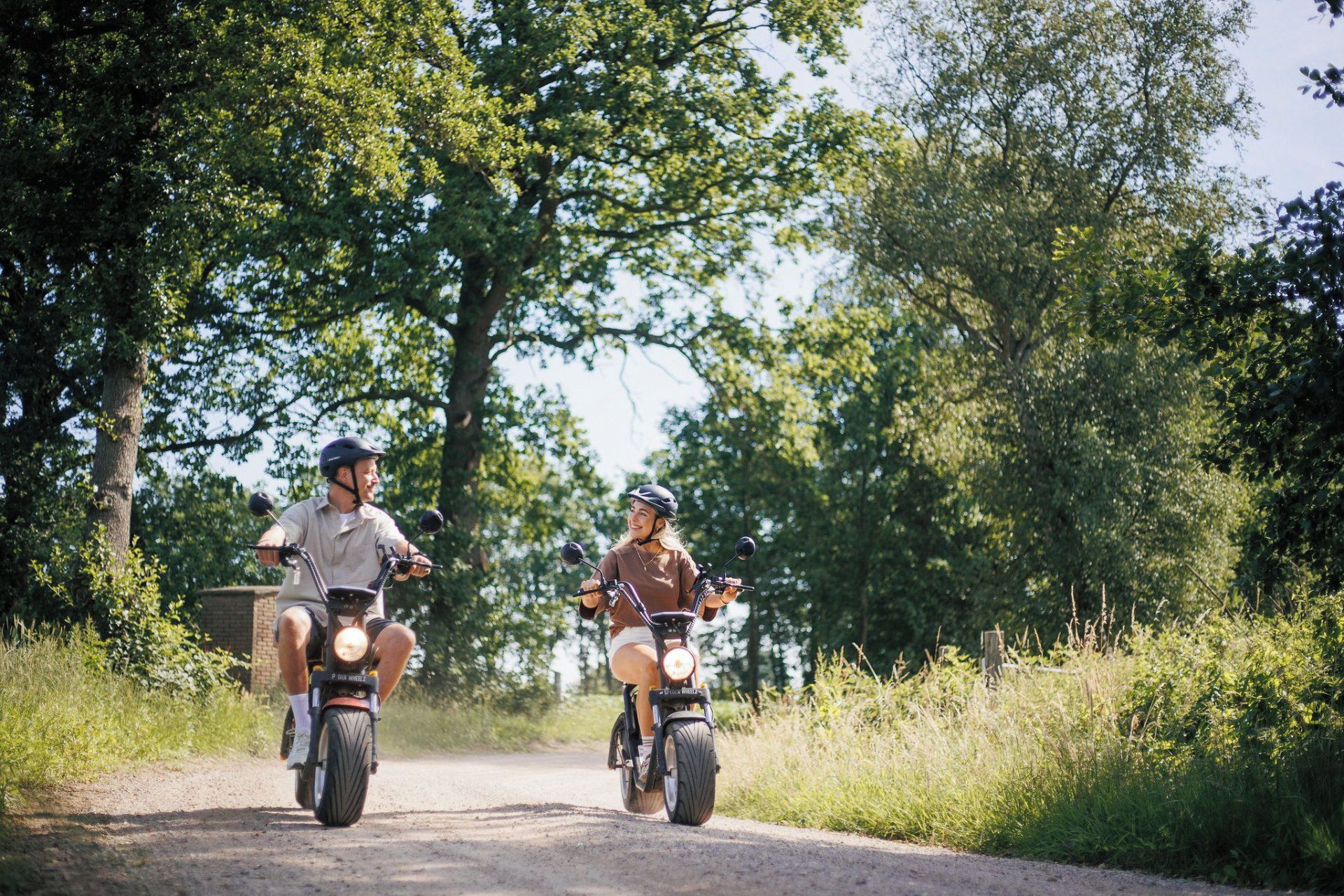 Two individuals on a dirt road, each riding a motorcycle.