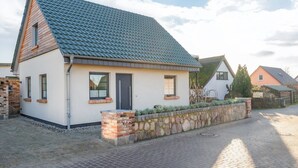 A single-story house with a sloped roof, a stone wall in front, and a paved driveway. - Villa Alma in Loddin - with balcony and terrace and charging station for e-bikes (Loddin)