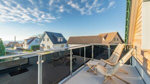 A balcony with a glass railing, wooden chairs, and a view of neighboring houses. - Villa Alma in Loddin - with balcony and terrace and charging station for e-bikes (Loddin)
