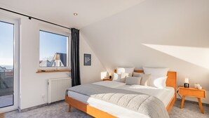 A bedroom with a large bed, a window with a view, a bedside table with a lamp, and a radiator. - Villa Alma in Loddin - with balcony and terrace and charging station for e-bikes (Loddin)