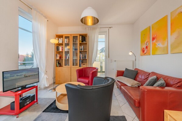 Un salon moderne avec un canapé rouge, un fauteuil noir, un meuble de rangement rouge et une bibliothèque.