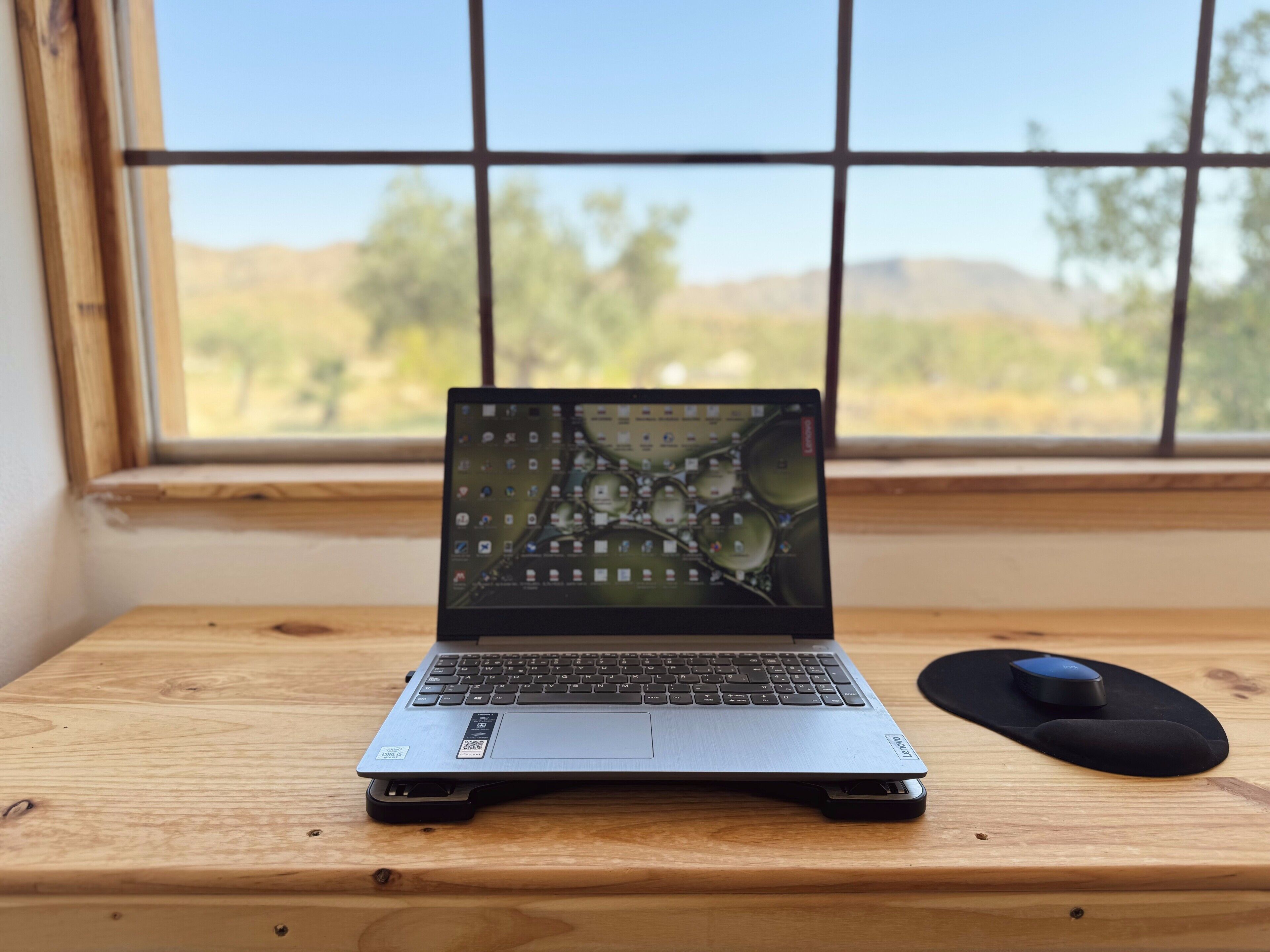 Un ordinateur portable est posé sur un bureau en bois, avec une fenêtre en arrière-plan.