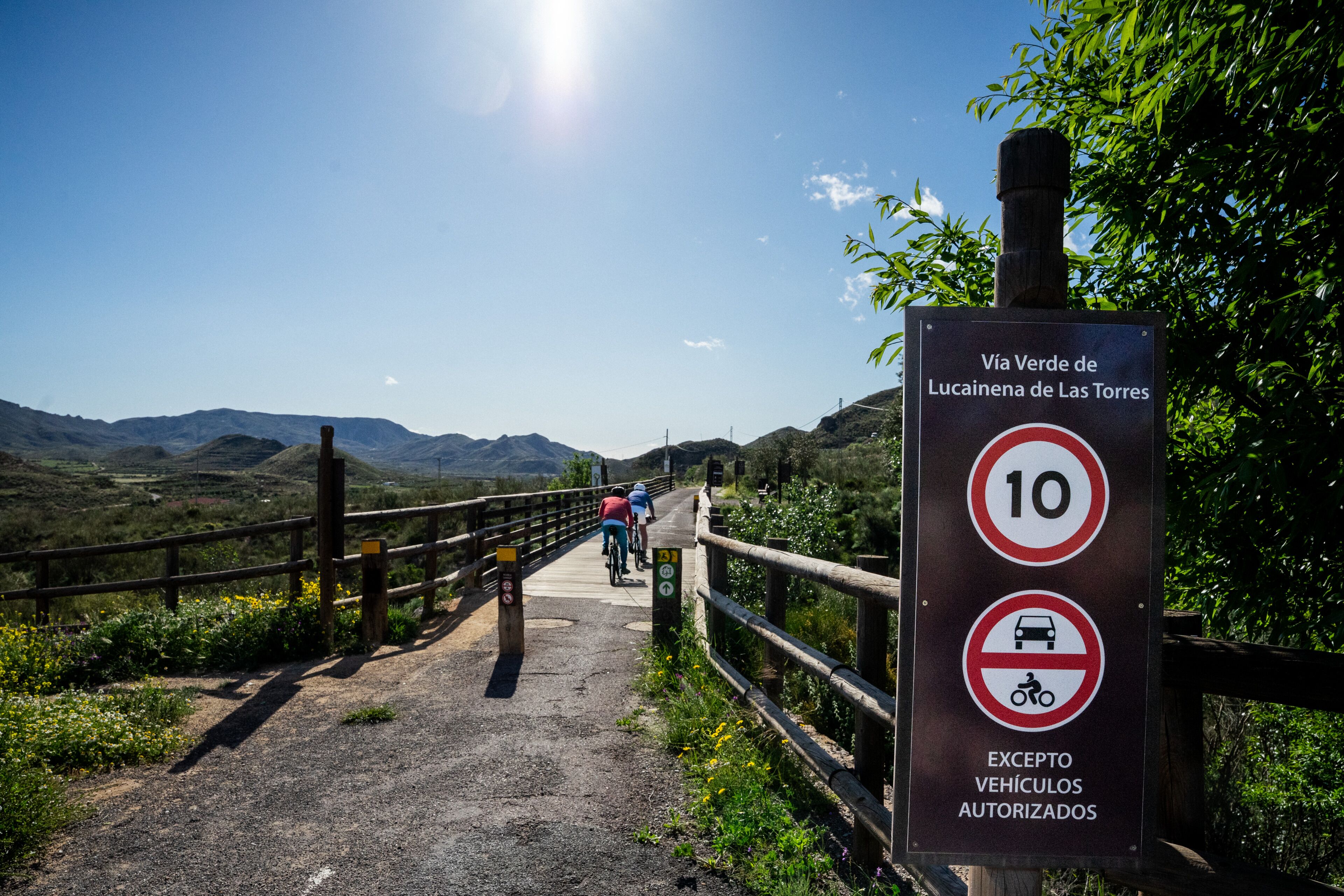 A sign indicating a 10 km/h speed limit on a scenic mountain path with cyclists.