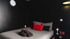 A modern bedroom with a bed, pillows, a clock, and bedside lamps. - Charming Cosy Studio in Saint-Denis-Stade de France (Saint-Denis)