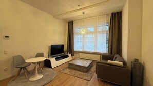 Ein modernes Wohnzimmer mit Flachbildfernseher, einer Couch, einem Couchtisch und einem Essbereich mit einem Stuhl.