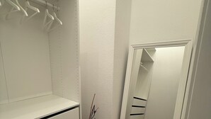 Ein begehbarer Kleiderschrank mit offenen Regalen, einer Kleiderstange und einer Spiegelklappe.