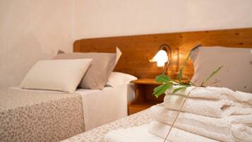 Quarto com cabeceira de madeira, cama com travesseiro branco, mesa de cabeceira com abajur e uma pilha de toalhas brancas.