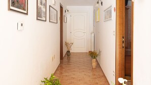 Een gang met betegelde vloer, foto's aan de muur, een deur aan het einde en een plant aan de linkerkant.
