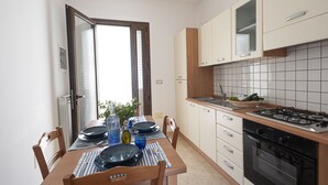 A kitchen with a dining table set for two, a stove, and cabinets. - Mirto Apartment with Private Terrace, Wi-Fi and Air Conditioning (Gagliano del Capo)