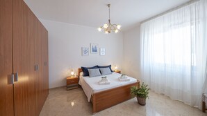 A bedroom with a wooden bed, bedside tables, a chandelier, a potted plant, and sheer curtains. - Mirto Apartment with Private Terrace, Wi-Fi and Air Conditioning (Gagliano del Capo)
