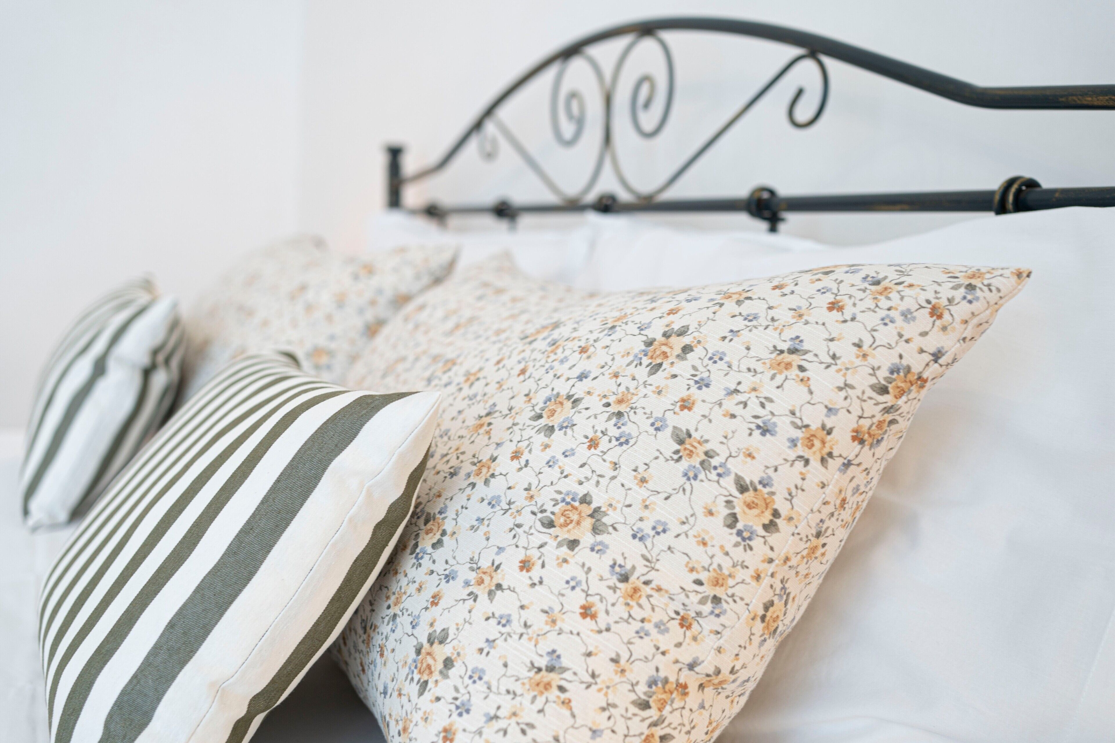 Un lit avec une tête de lit en métal, un oreiller à rayures et un oreiller à motifs floraux.