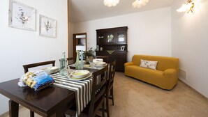 Un coin repas avec une table dressée pour deux personnes, un canapé jaune et un meuble en arrière-plan.