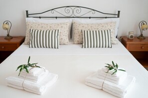 Ein ordentlich bezogenes Bett mit floralen und gestreiften Kissen, zwei Nachttische mit Lampen und Bettwäsche mit Pflanzenmuster.