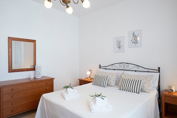 A bedroom with a bed, a wooden dresser, a nightstand with a lamp, and wall art.