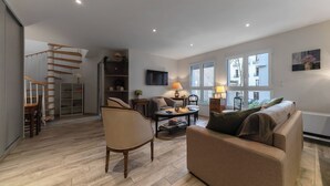 A spacious living room with a staircase, a sofa, a coffee table, and a TV.