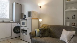 A compact living space with a sofa, a small table, a washing machine, a microwave, and a pendant light. - Appartement Cosy en centre ville avec parking (Clermont-Ferrand)