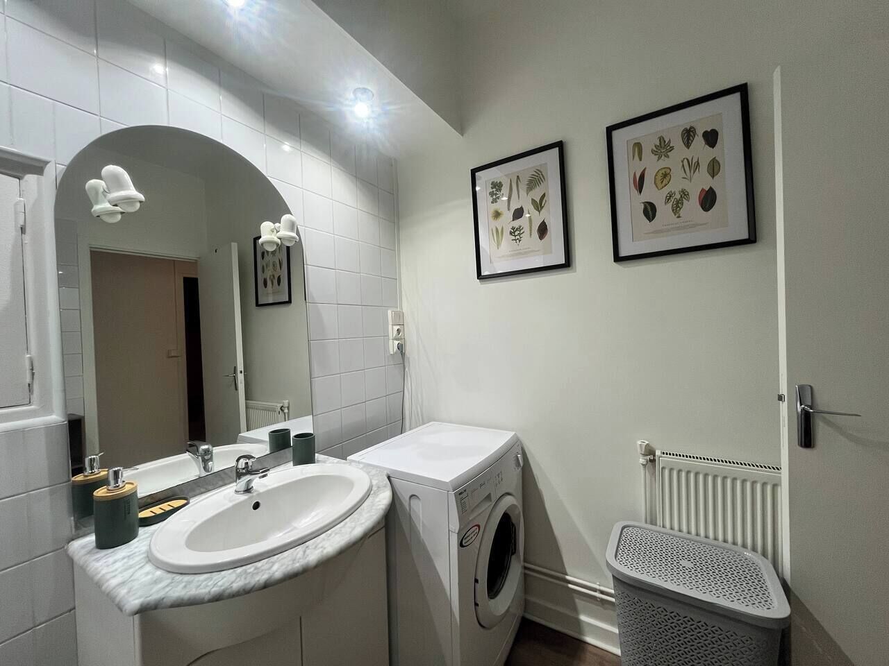 A modern bathroom with a sink, mirror, washing machine, and a radiator.