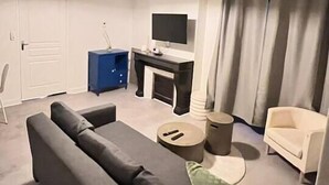A modern living room with a grey sofa, a small coffee table, a TV on a stand, and a blue cabinet. - Appartement Cosy en centre ville (Clermont-Ferrand)