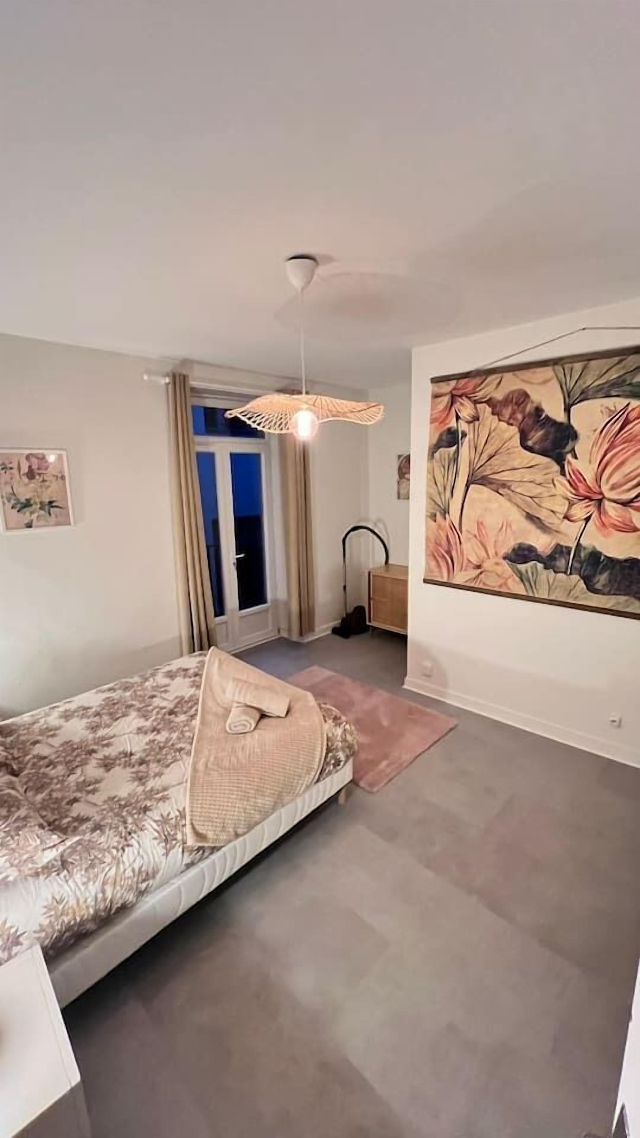 Ein Schlafzimmer mit einem Bett, einem Deckenventilator, einem Gemälde und einer Tür, die auf einen Balkon führt.