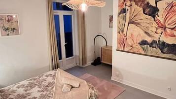 Ein Schlafzimmer mit einem Bett, einem Deckenventilator, einem Gemälde und einer Tür, die auf einen Balkon führt.