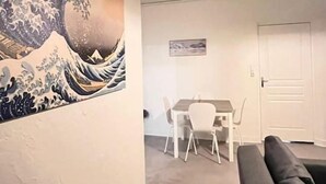 A living room with a large Japanese wave painting, a gray sofa, a dining area with a table and chairs, and a door in the background. - Appartement Cosy en centre ville (Clermont-Ferrand)
