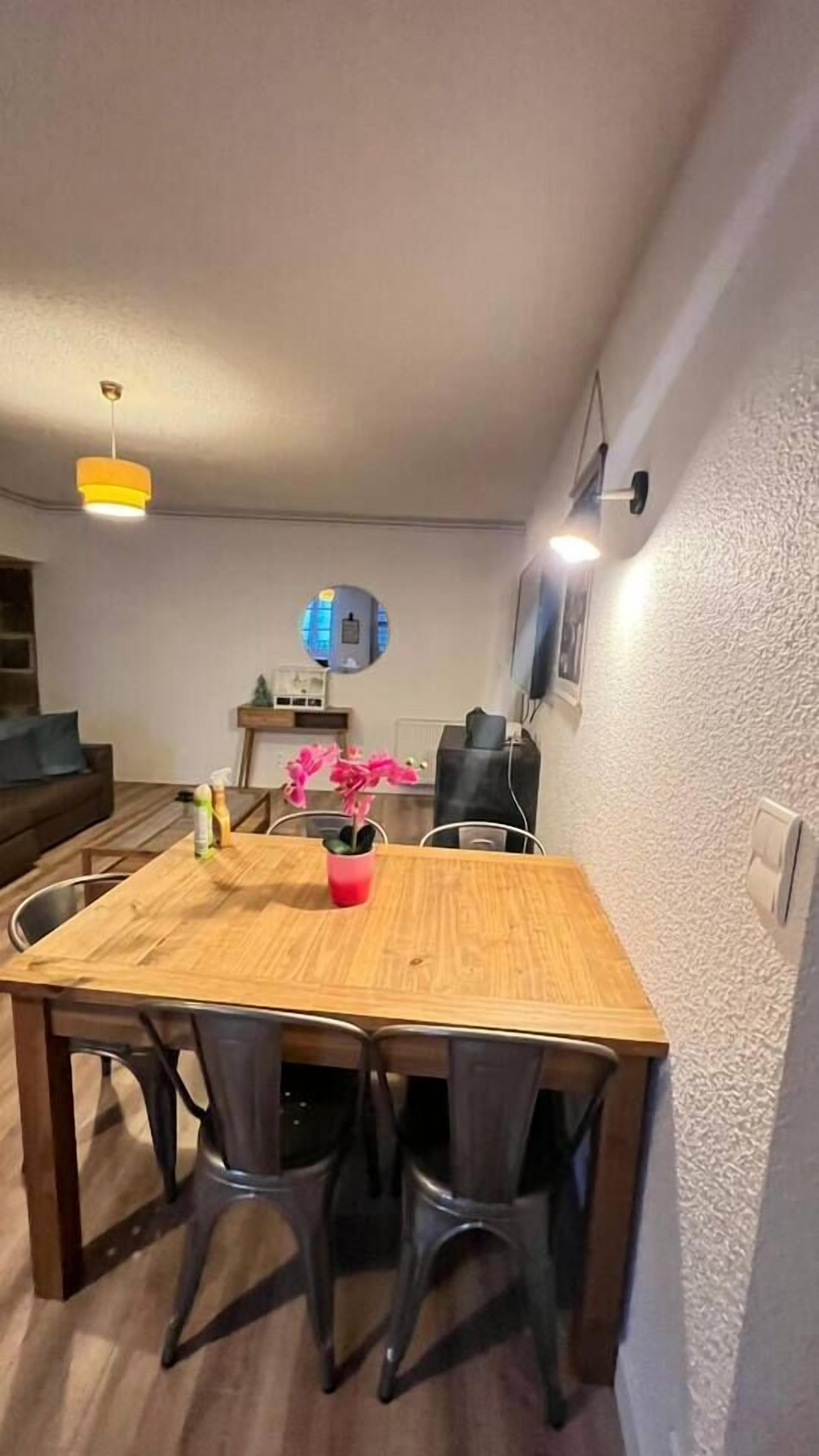 A dining area with a wooden table and four chairs, a small potted plant, and a coffee machine.