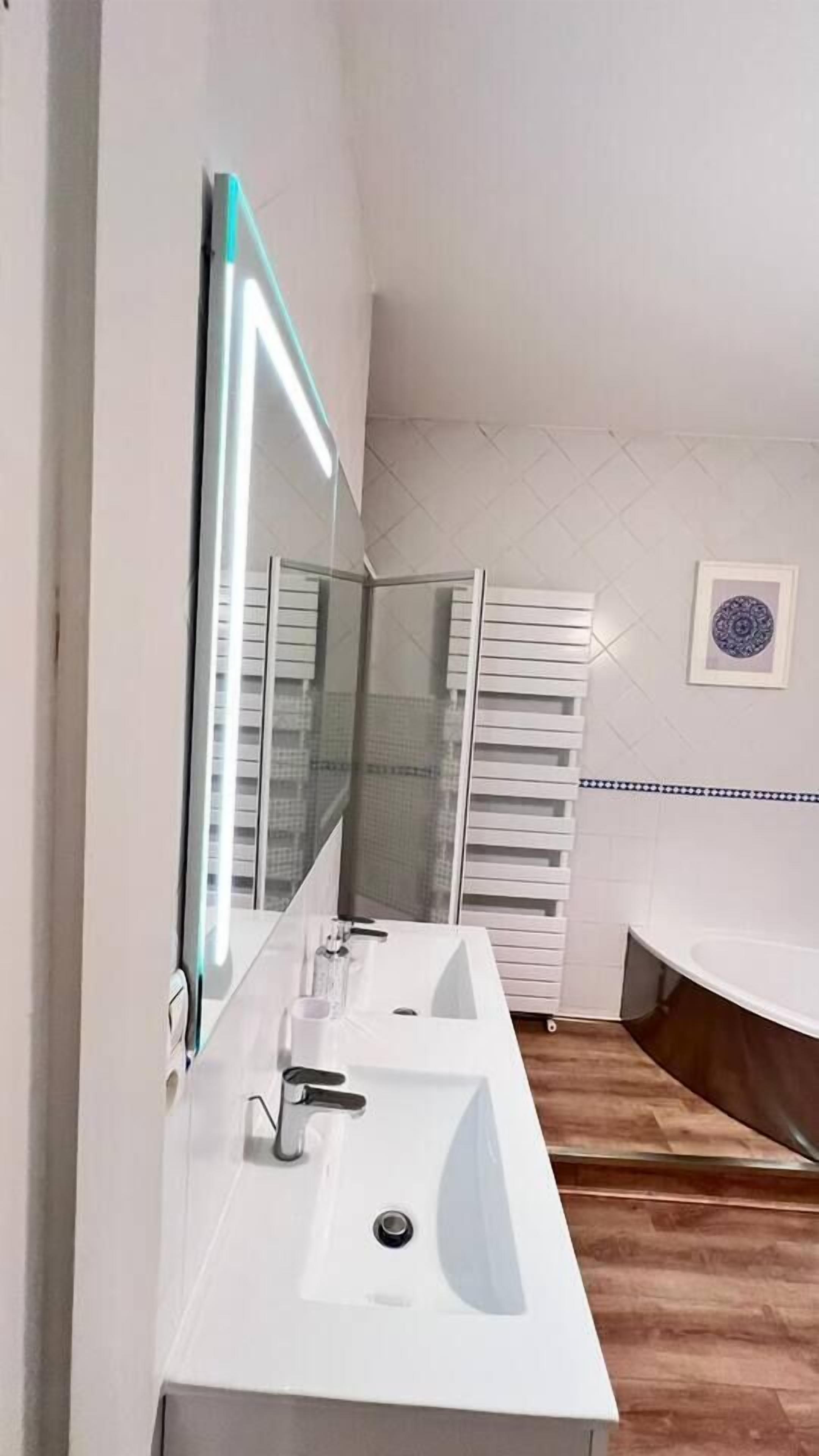 Ein modernes Badezimmer mit einem großen Spiegel, zwei Waschbecken und einer Badewanne.