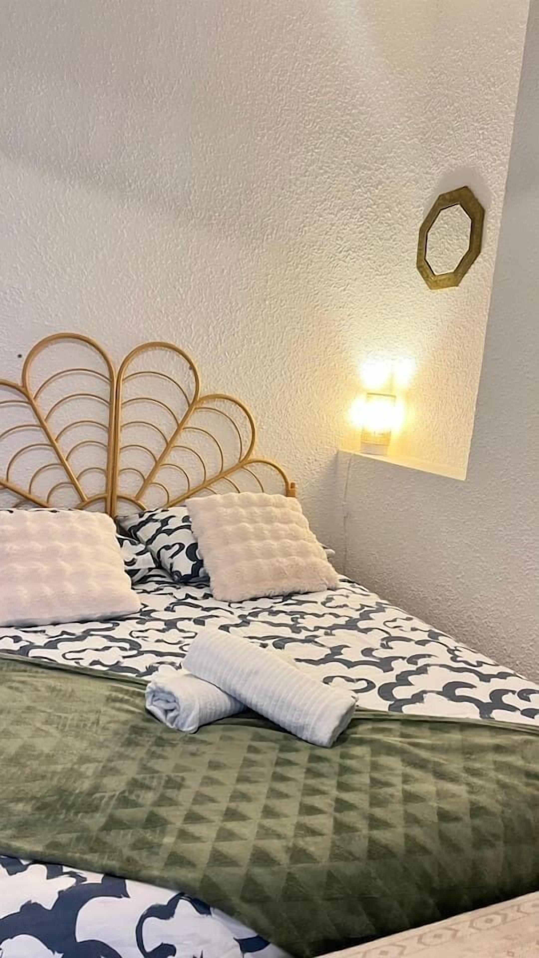 A neatly made bed with patterned bedding, a decorative headboard, and a wall-mounted light fixture.