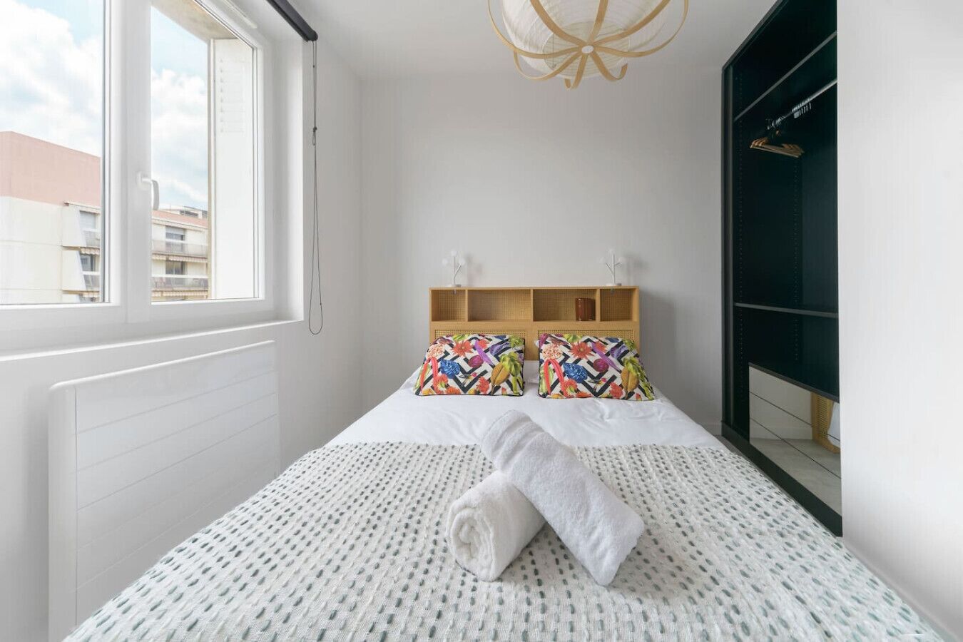 Une chambre moderne avec un grand lit, une tête de lit en bois, une fenêtre et un luminaire suspendu.