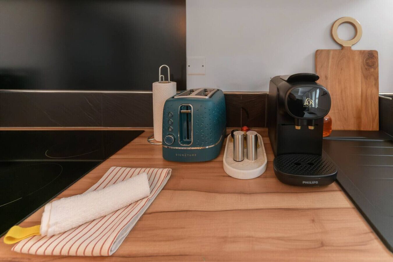 A kitchen counter with a toaster, a coffee maker, a paper towel holder, and a striped cloth.